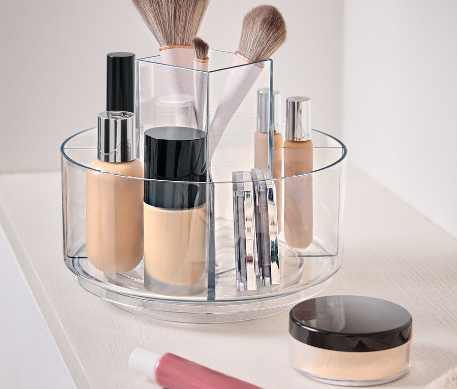 Durchsichtiger, drehbarer Behälter mit Kosmetika auf einer weißen Oberfläche.