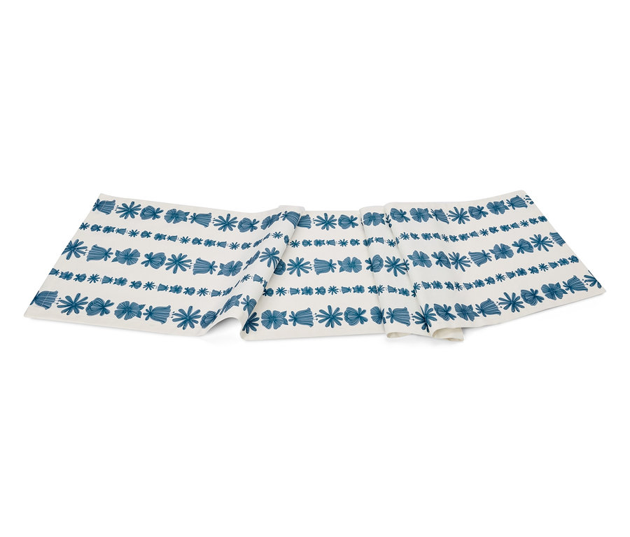 Weißer Tischläufer mit blauem Muster aus Blumen und geometrischen Formen.