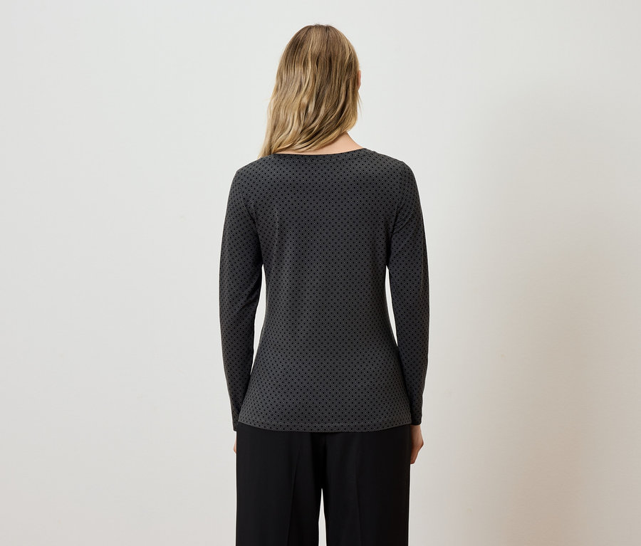 Eine Frau mit dem Rücken zur Kamera trägt eine grau-schwarze Bluse mit langen Ärmeln und eine schwarze Hose.