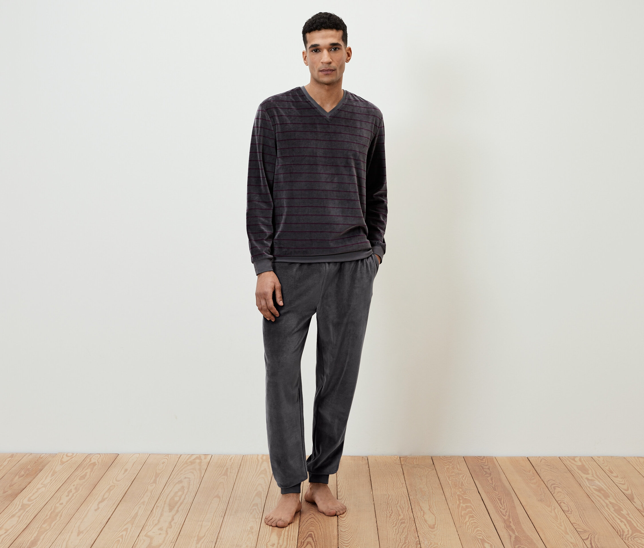 Mann steht barfuß und trägt einen grauen, gestreiften Velours-Pyjama.