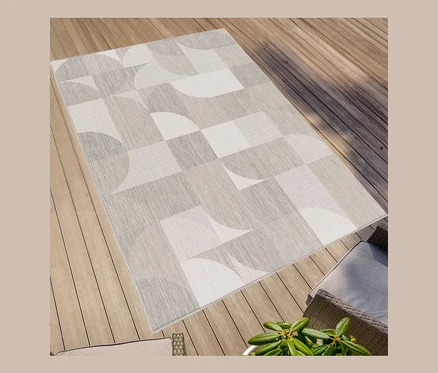 Ein faltbarer Outdoor-Teppich im geometrischen Design liegt auf einem Holzboden.