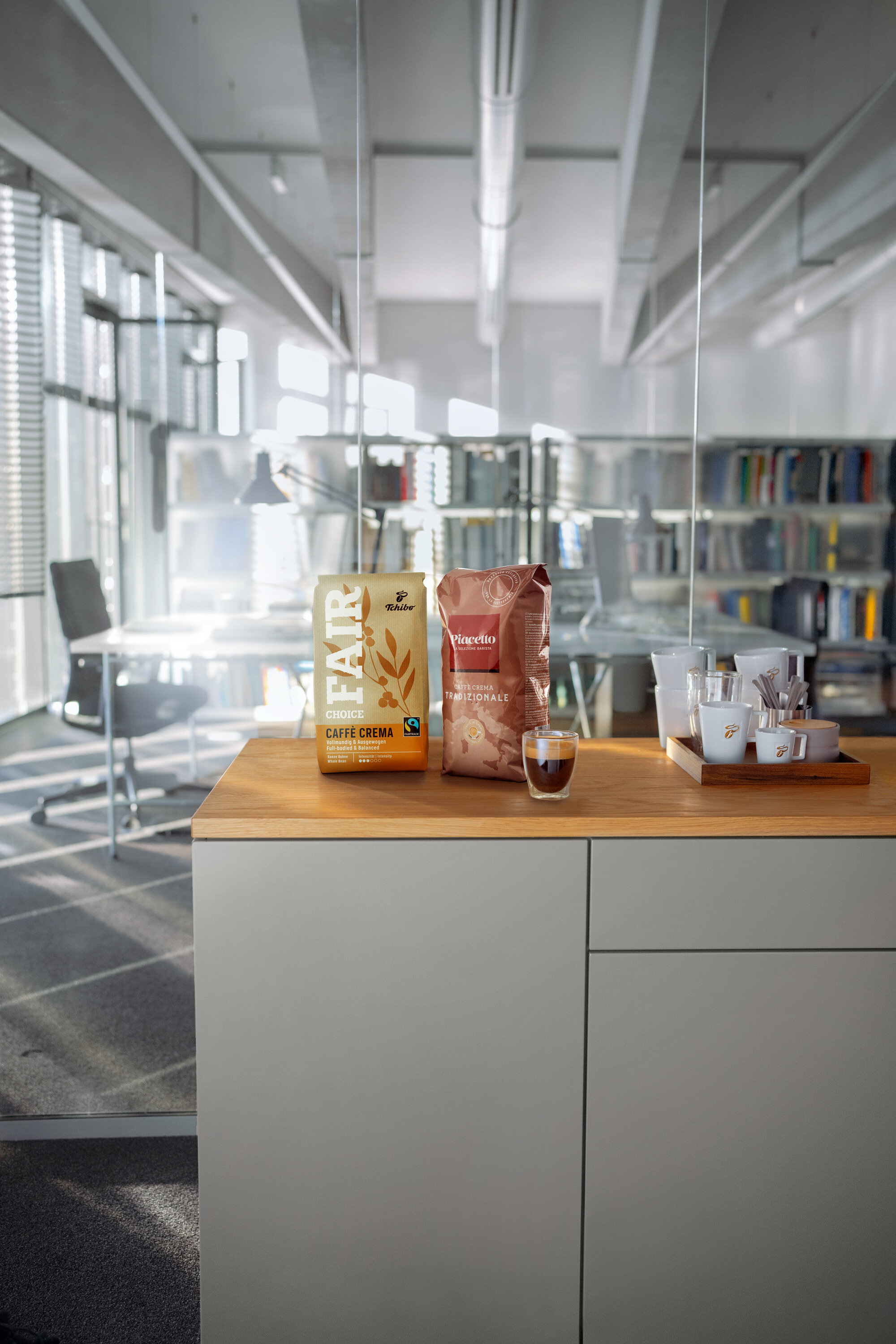 Zwei Kaffeepackungen und eine Tasse Espresso auf einer Holzplatte in einem modernen Büro.