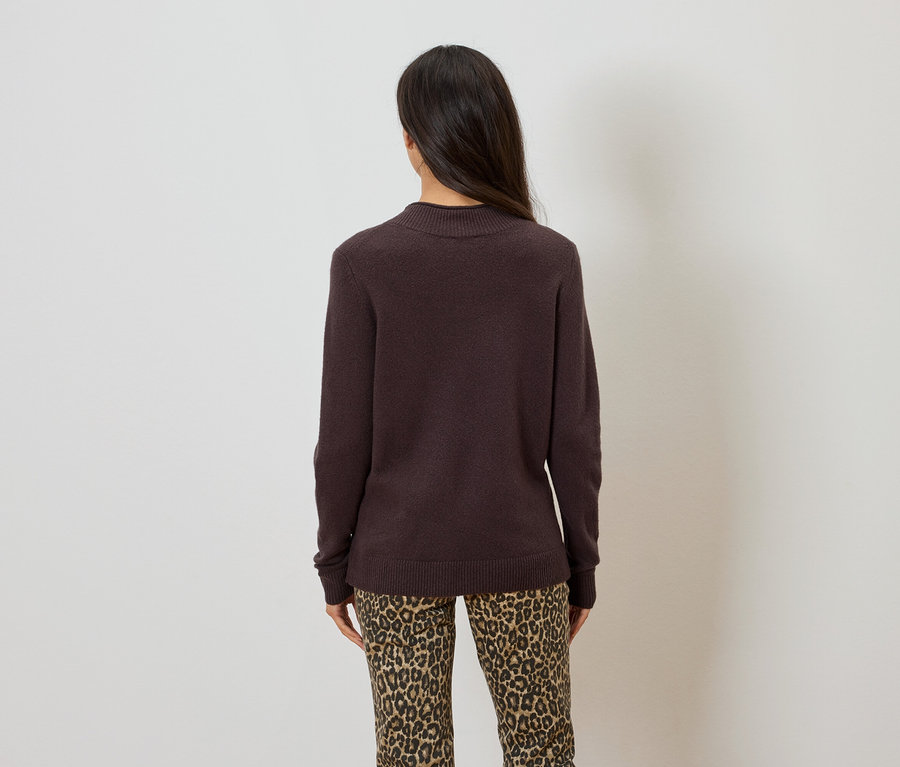 Rückansicht einer Frau mit langen, dunklen Haaren, die einen dunkelbraunen Pullover und eine Hose mit Leopardenmuster trägt.