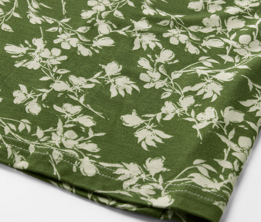 Detailansicht eines bedruckten Blusenshirts mit Blumenmuster auf grünem Stoff.
