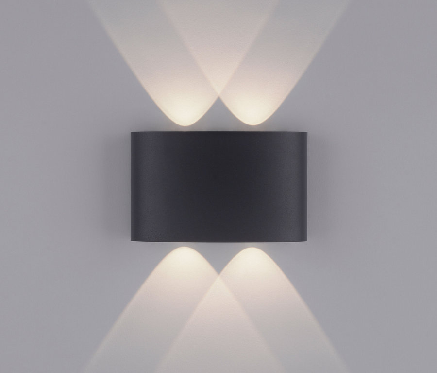 Eine schwarze Paul Neuhaus LED-Outdoor-Wandleuchte »Carlo« strahlt an einer grauen Wand Lichtstrahlen nach oben und unten.