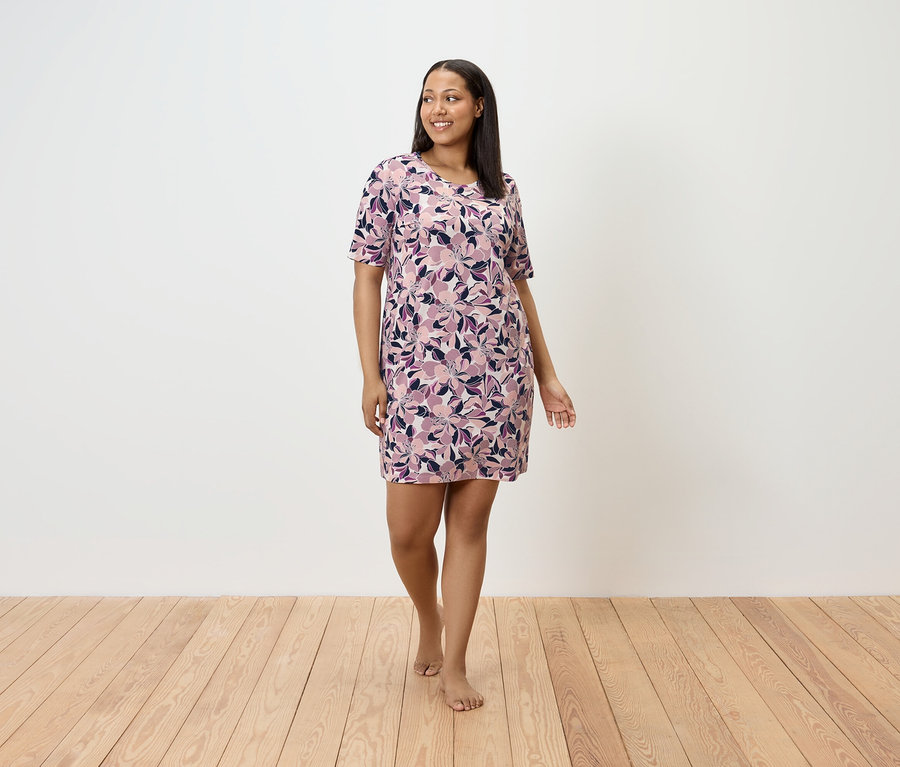 Eine barfuß gehende Frau trägt ein geblümtes Kleid und geht über einen Holzboden.