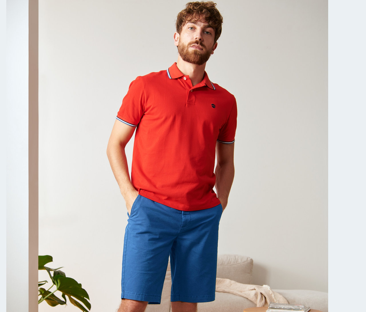 Mann posiert in rotem Poloshirt und royalblauen Chino-Shorts.