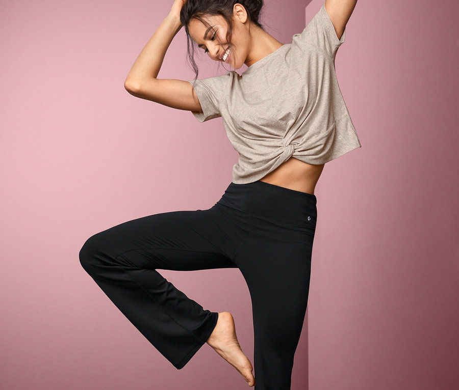 Frau steht auf einer Yogamatte und trägt ein Sportshirt.