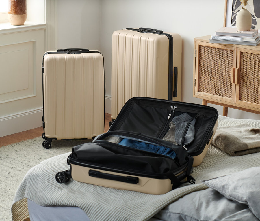 Drei recycelte Hartschalen-Koffer in Beige stehen im Raum, einer ist auf dem Bett geöffnet.