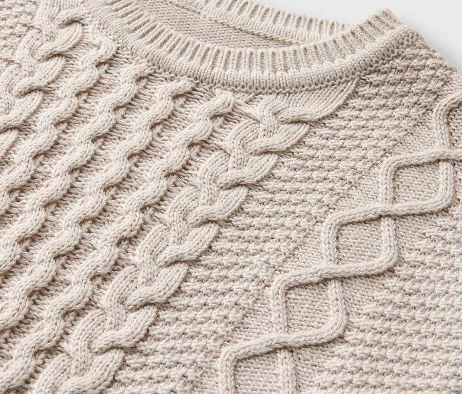 Detailaufnahme eines cremefarbenen Strickpullovers mit Zopfmuster.
