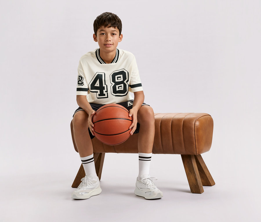 Ein Junge sitzt auf einer braunen Bank und hält einen Basketball.