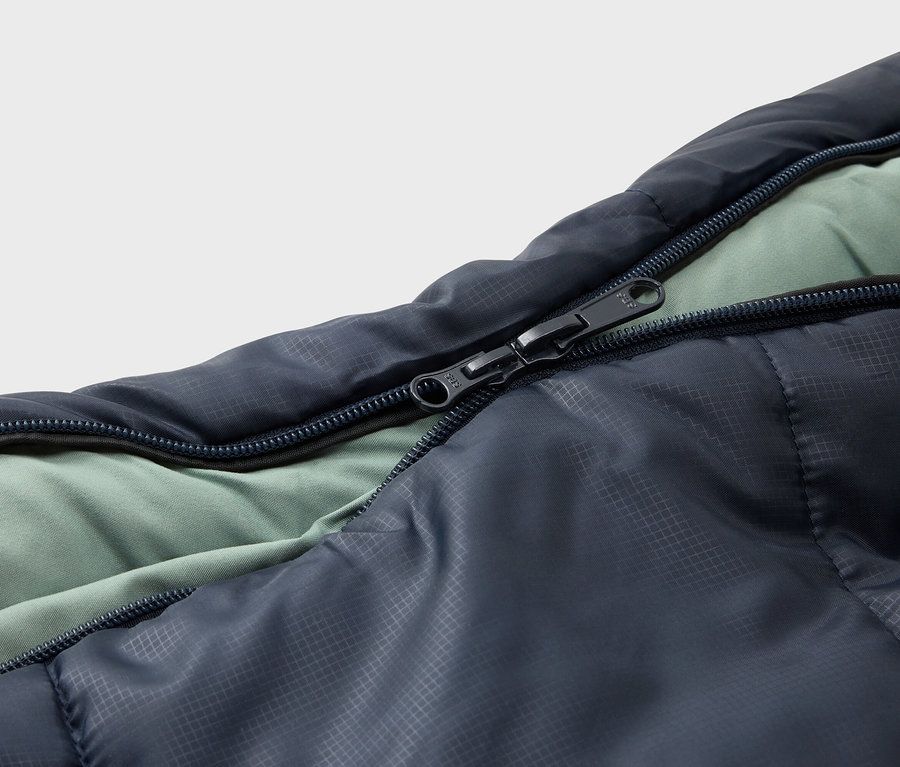Detailansicht eines geöffneten, marineblauen Schlafsacks mit hellgrünem Innenfutter und einem schwarzen Reißverschluss.
