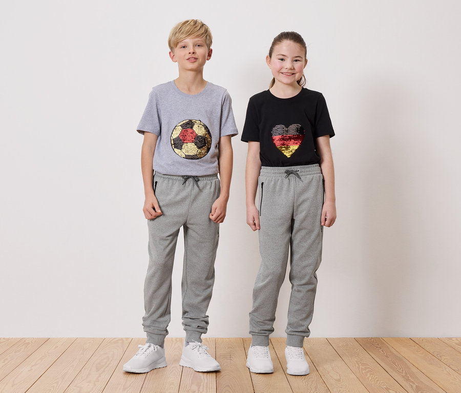 Ein Junge in einem grauen T-Shirt mit einem Fußball-Design und ein Mädchen in einem schwarzen T-Shirt mit einem Herz-Design, beide tragen graue Jogginghosen.