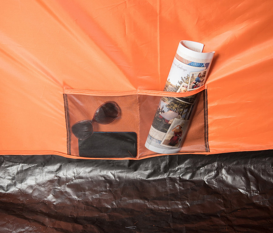 Innentasche eines orangefarbenen Zeltes mit Sonnenbrille, Handy und zusammengerollter Zeitschrift.