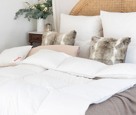 Nahaufnahme eines Bettes mit weißer "Paradies Winter-Daunendecke »Hoheluft«" in Normalgröße, weißen Kissen und dekorativen Kissen.
