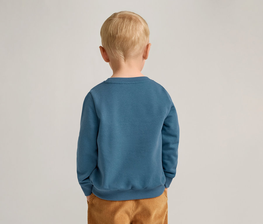 Rückansicht eines Kindes mit blonden Haaren, das ein blaues Sweatshirt und braune Cordhosen trägt.
