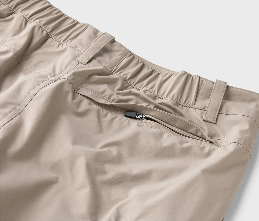Nahaufnahme einer beigen Hose mit elastischem Bund und Reißverschlusstasche.