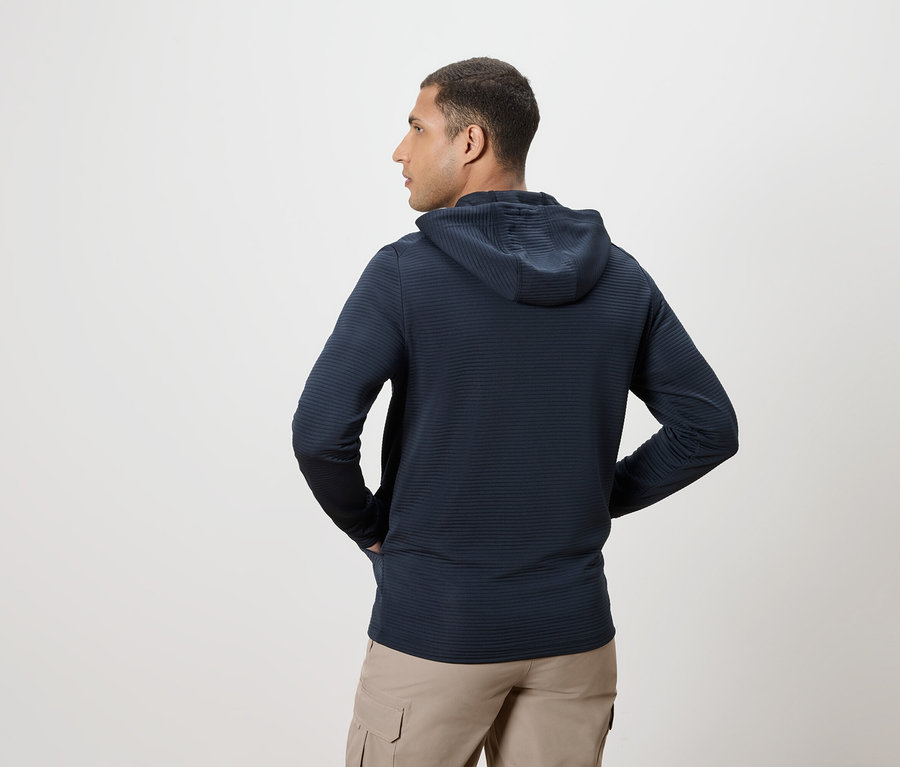 Mann von hinten in dunkelblauem Hoodie und beigen Hosen, Hände in den Taschen.