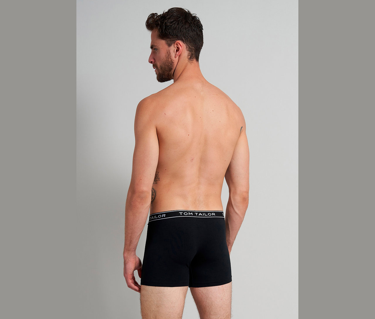 Mann von hinten, mit Tätowierungen, trägt schwarze Tom Tailor Boxershorts.