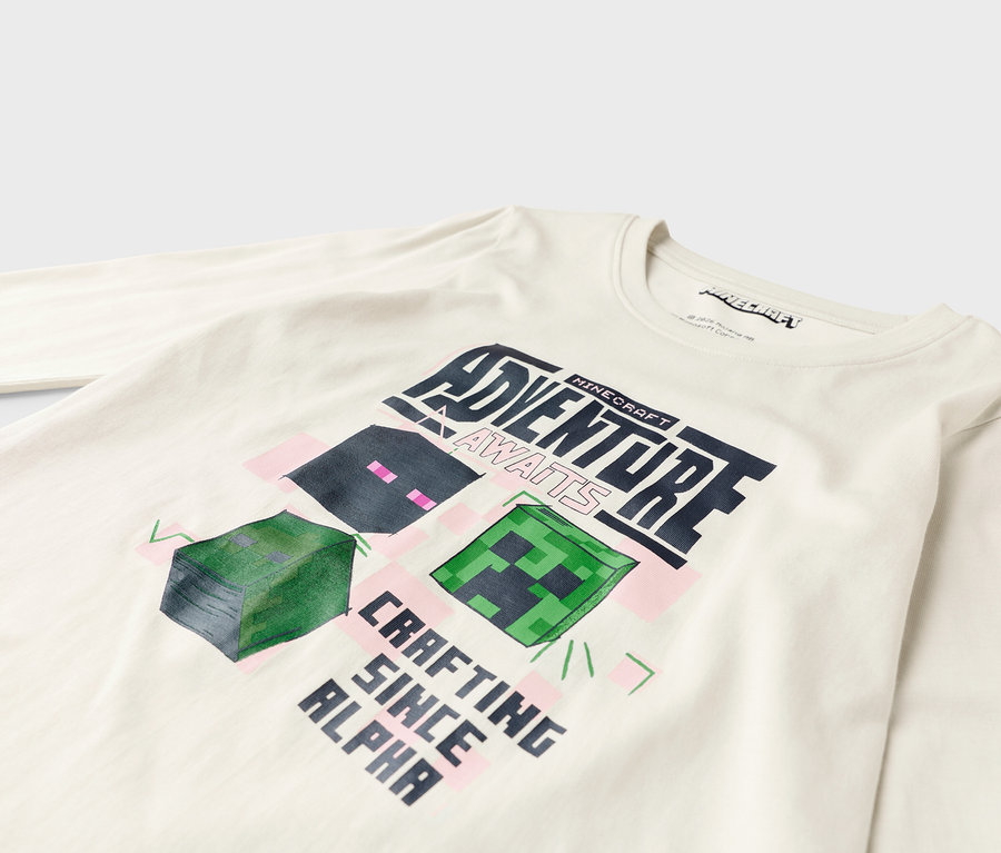 Auf einem weißen, langärmeligen Hemd ist ein Minecraft-Design mit der Aufschrift "Adventure Awaits" und "Crafting Since Alpha" abgebildet.