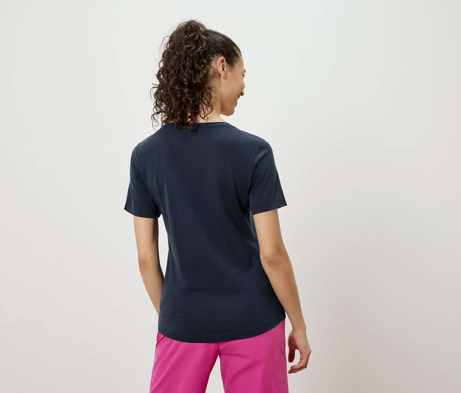 Rückansicht einer Frau mit lockigem Haar, die ein marineblaues T-Shirt und pinkfarbene Shorts trägt.