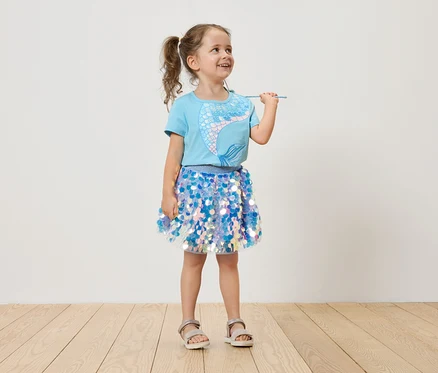 Mädchen mit Zöpfen, hellblauem Meerjungfrauen-T-Shirt und blauem Paillettenrock, das einen Zauberstab hält.
