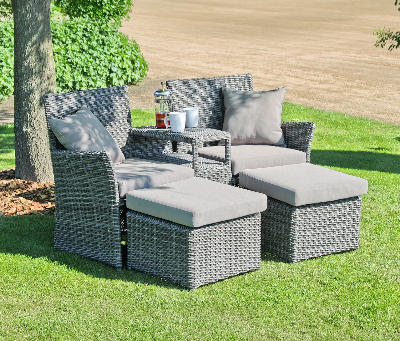 Graue Korbmöbel mit Kissen und Fußhocker stehen auf einer Rasenfläche. Auf dem Tisch stehen eine Teekanne und zwei Tassen.