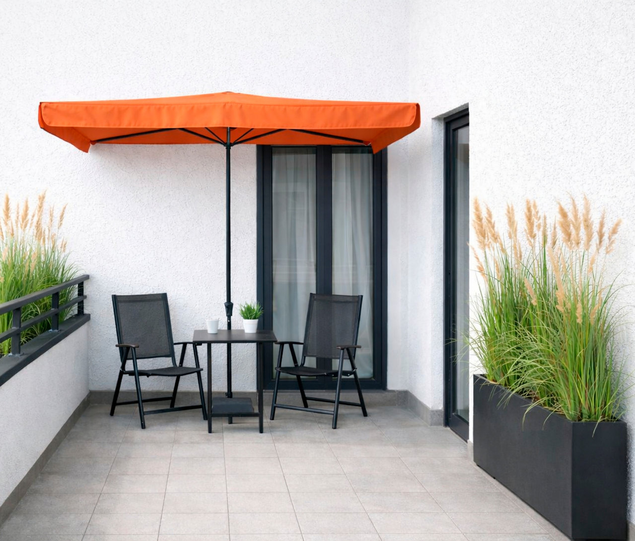 Terrasse mit Tisch, zwei Stühlen und einem orangefarbenen Sonnenschirm.