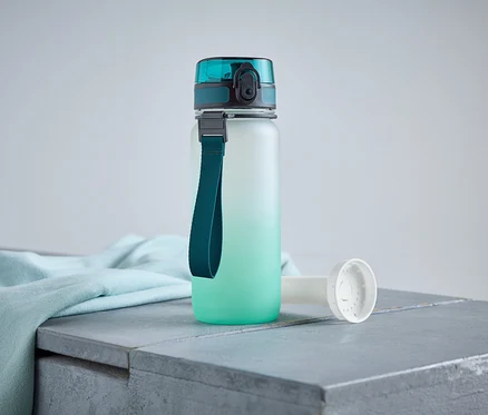 Eine Wasserflasche mit blaugrünem Deckel und Trageband steht auf einer grauen Oberfläche neben einem hellblauen Tuch.