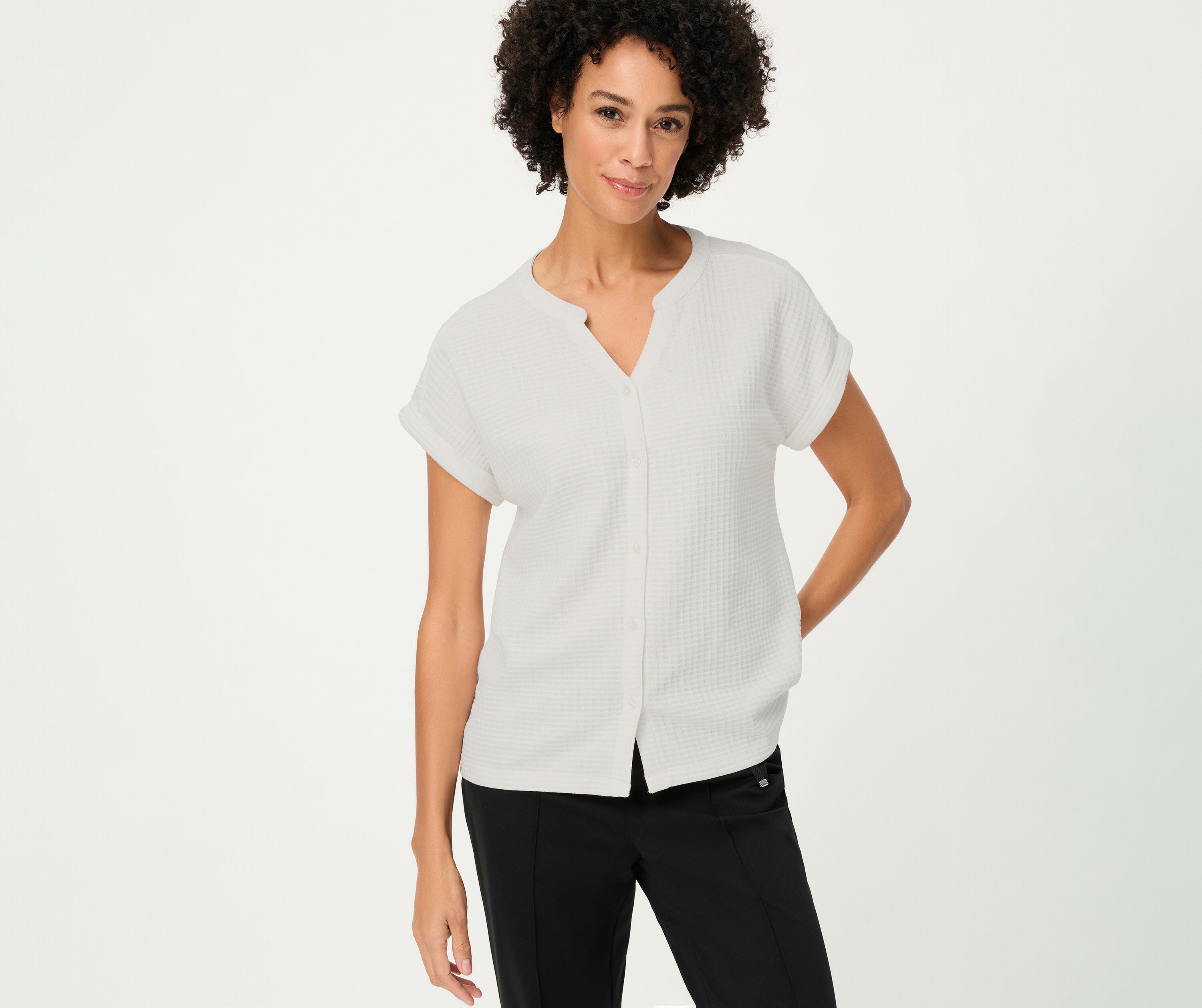 Frau mit lockigem Haar trägt ein strukturiertes Olsen Shirt mit Knöpfen in Weiß und schwarze Hose.