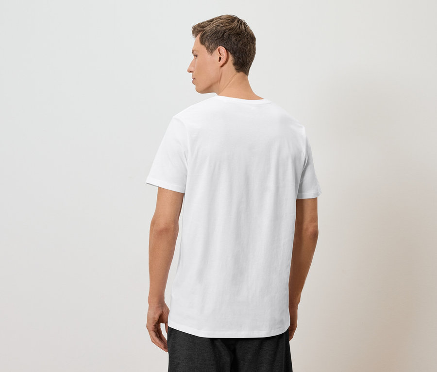 Ein Mann steht mit dem Rücken zur Kamera und trägt ein weißes T-Shirt und dunkle Shorts.