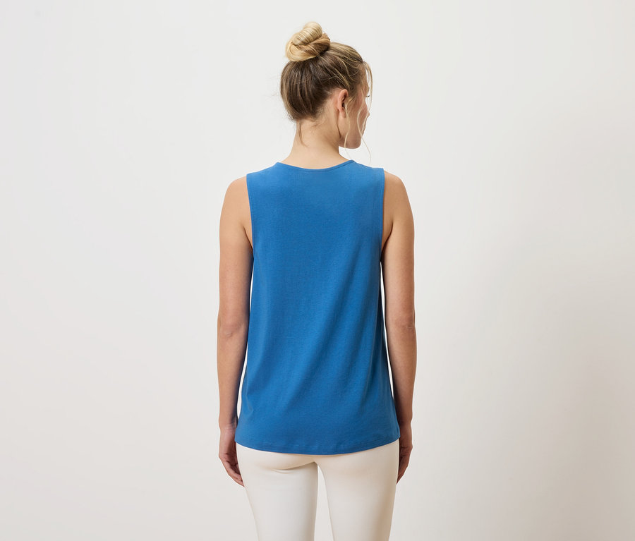 Rückansicht einer Frau mit einem Dutt, die ein blaues Tanktop und weiße Hosen trägt.