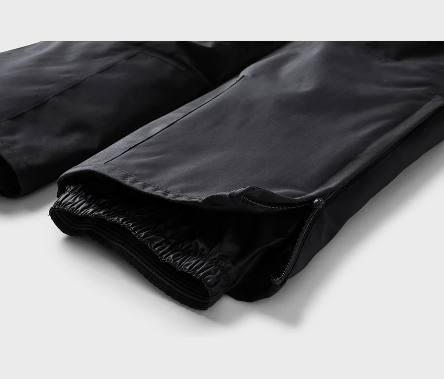 Nahaufnahme des Knöchelbereichs einer schwarzen Hose mit teilweise geöffnetem Reißverschluss, der ein elastisches Innenbündchen zeigt.