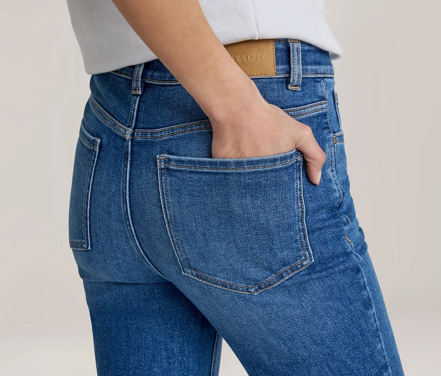 Nahaufnahme des Rückens einer Person in blauen Jeans, eine Hand steckt teilweise in der rechten Gesäßtasche. Ein braunes "YSTYLE"-Etikett ist am Bund sichtbar.