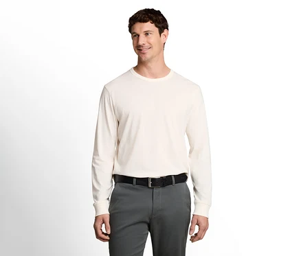 Mann in einem cremefarbenen Langarmshirt, dunkelgrauer Hose und schwarzem Gürtel, lächelt und blickt nach rechts.