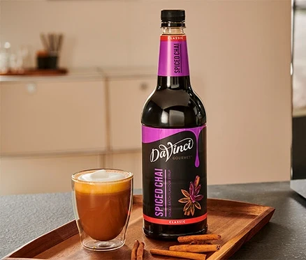 Ein Glas Chai Latte und eine Flasche DaVinci Spiced Chai Sirup auf einem Holztablett.