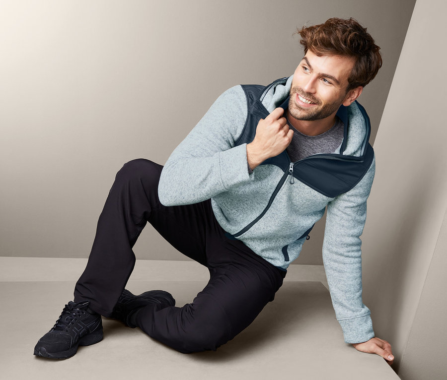 Mann sitzt am Boden und trägt eine Strickfleece-Jacke.