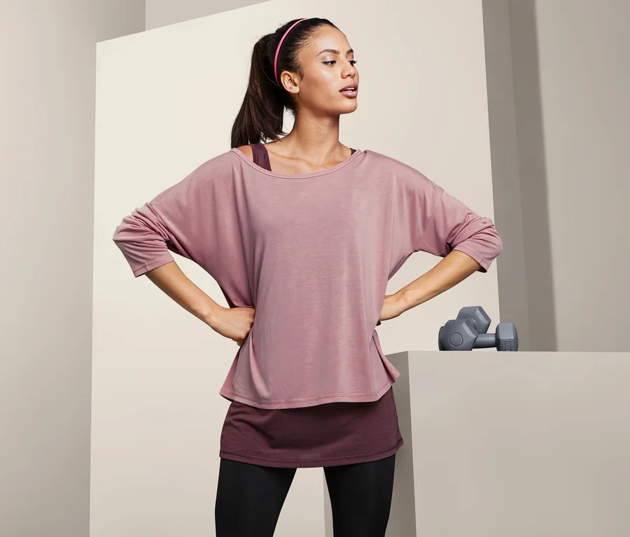 Frau posiert mit Händen in den Hüften in einem 2-in-1-Sportshirt.