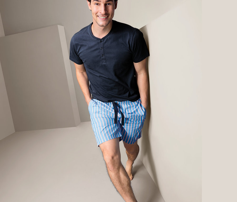 Ein Mann im Shorty-Pyjama steht in einer Ecke des Raumes.