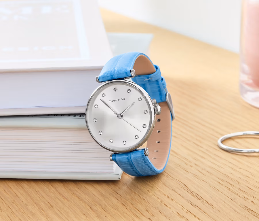 Eine Armbanduhr mit Lederband und Kristallen liegt auf Büchern.