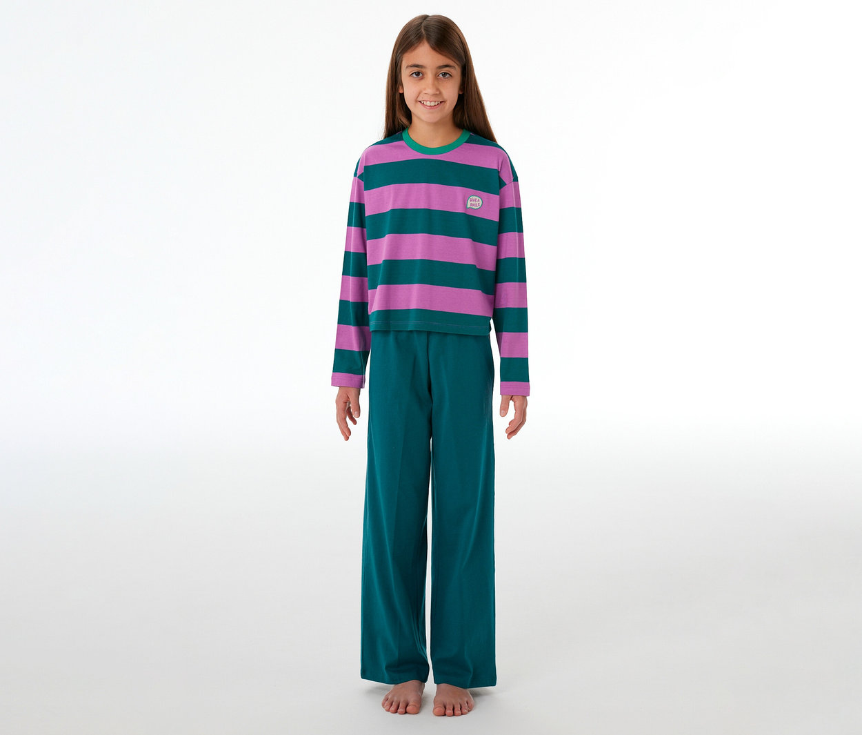 Ein junges Mädchen steht lächelnd barfuß in einem gestreiften SCHIESSER Kinder-Pyjama in Lila und Türkis mit passender Hose.