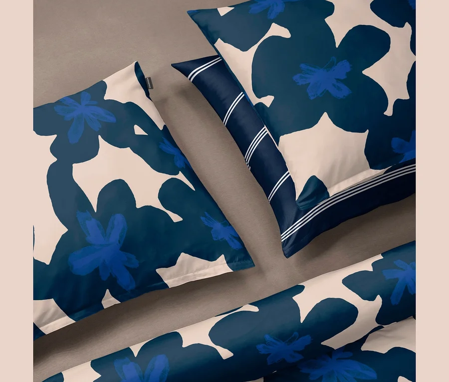 SCHIESSER Renforcé-Bettwäsche »Blossom« mit großem blauem Blumenmuster auf hellem Grund. Zwei Kissen und eine gerollte Decke, ein Kissen mit dunkelblauer gestreifter Bordüre.