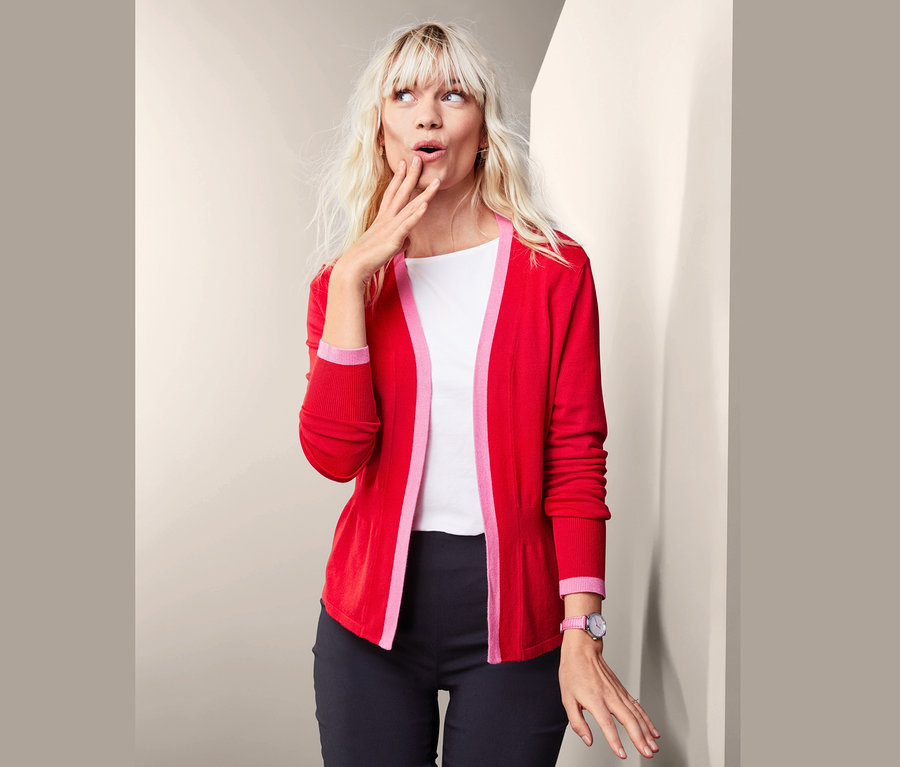 Blonde Frau posiert nachdenklich in offener, roter Feinstrickjacke.