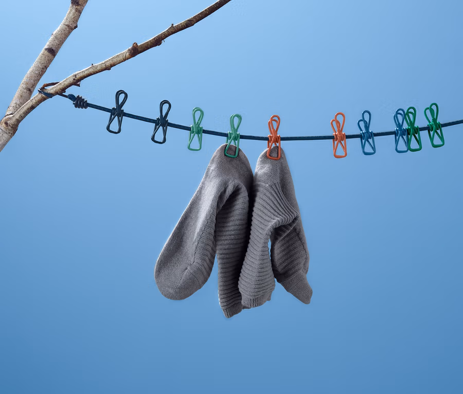 Zwei graue Socken hängen an einer Camping-Wäscheleine, die an einem Ast vor blauem Himmel befestigt ist.