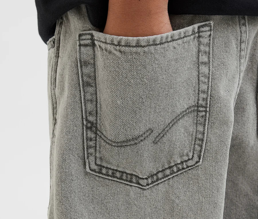 Eine Hand steckt in der Gesäßtasche einer grauen Jack&Jones JJOrginial Alex Jeans.