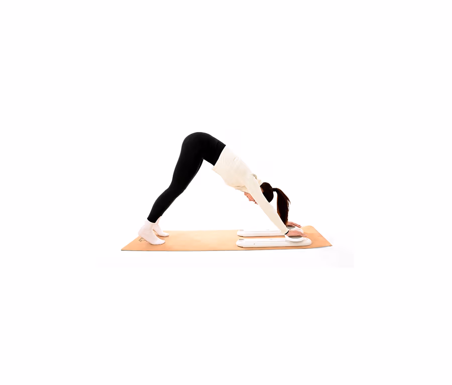 Frau in schwarzer Leggings und weißem Oberteil macht die Yoga-Pose Herabschauender Hund auf einer Yogamatte, mit weißen Fitness-Gleitern unter den Händen.
