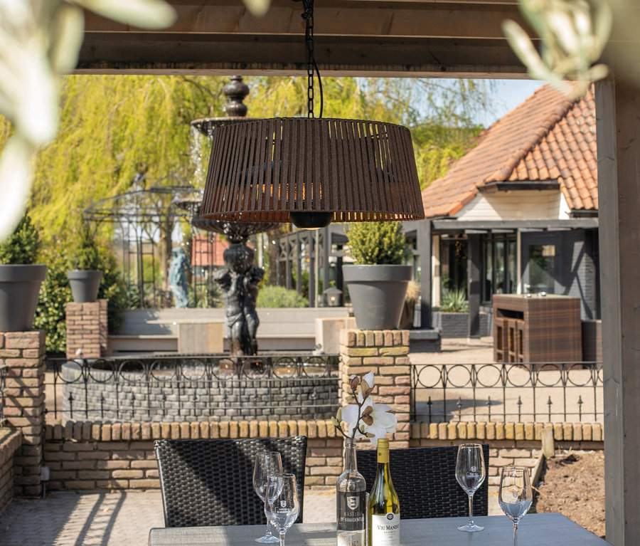 Außensitzbereich mit Blick auf einen Brunnen, über dem Tisch hängt ein brauner Sunred-Hänge-Heizstrahler »Halogen Artix Corda«.