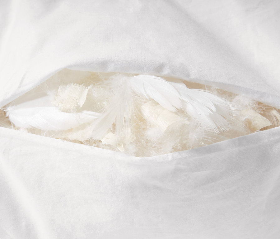 Detailansicht eines weißen Zirbenkopfkissens, teilweise geöffnet, das Federn und Füllung zeigt.