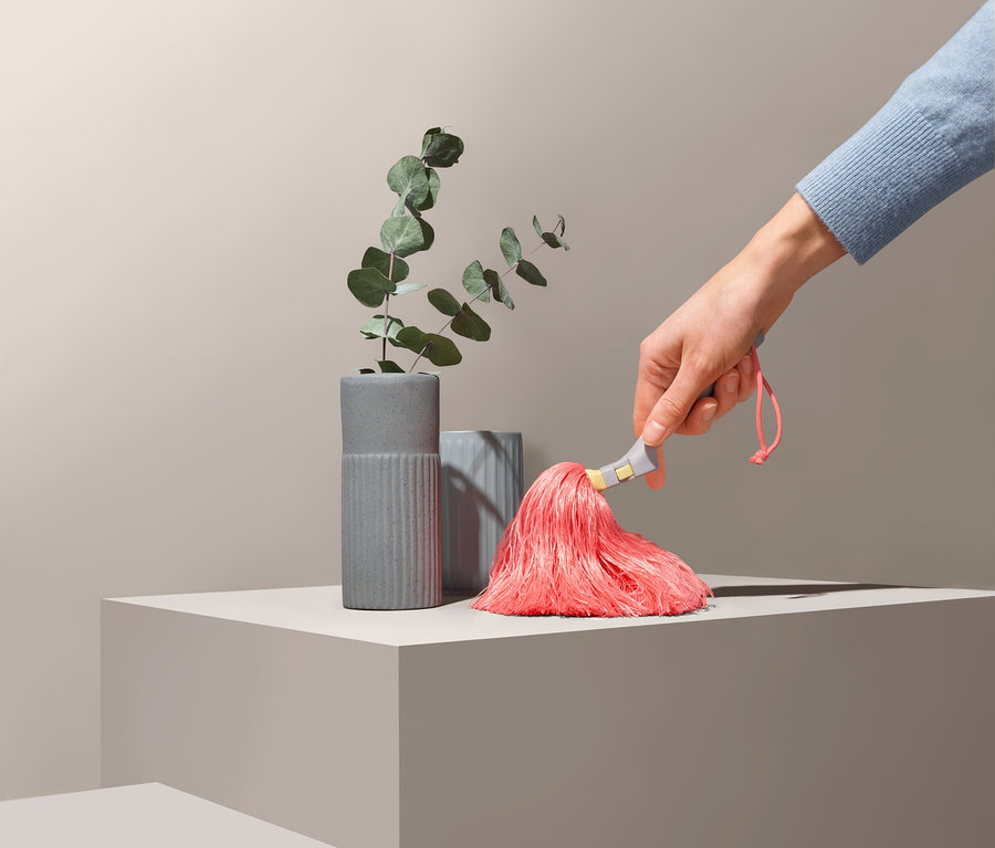 Eine Hand hält ein Staubschwert und -wedel neben grauen Vasen und Eukalyptus.