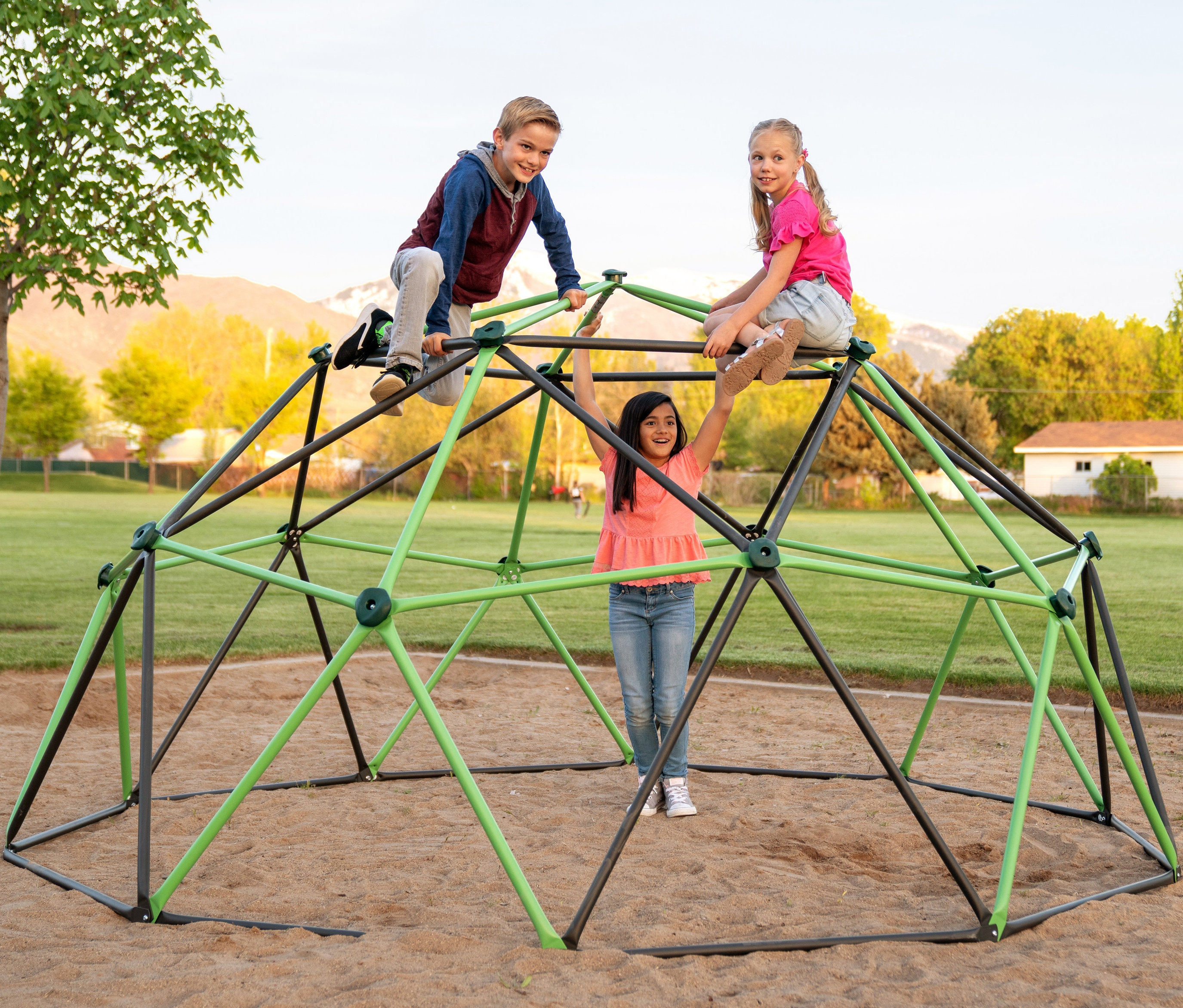 Drei Kinder spielen auf einem großen, schwarz-grünen LIFETIME-Klettergerüst »Geodome« auf einem Sandplatz.